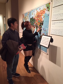 Chengkun Huang, a scientist physicist at Los Alamos (and a state resident), with his sister in-law  Ying Xiong, visiting from Guangzhou, China, as she places a dot to show her place of birth in MOIFA's Gallery of Conscience [photo by Interim Director Charlene Cerny]